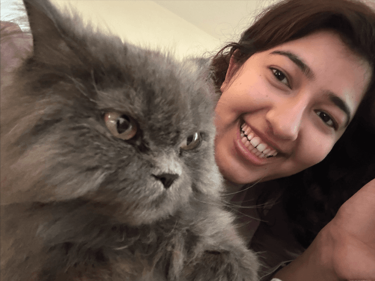 Akansha laughing, cheek to cheek with Gracie, a fluffy grey cat